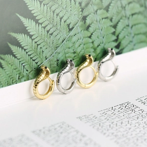 Detail of cobra huggie earrings in gold and silver finish with scaled texture and dark eyes