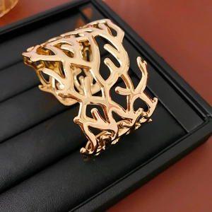 Detail of a wide gold-plated open cuff bracelet with an intricate hollow coral branch design