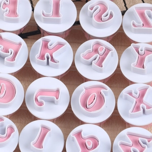 Close-up of 26 pieces alphabet cookie cutters set with pink letter stamps in white base