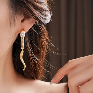 Macro shot of gold snake-shaped earrings with zircons on a model's ear detail
