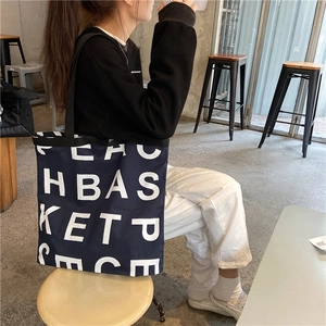 Large black canvas tote bag with white letter print shown in a lifestyle cafe setting