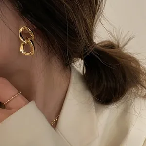 Dettaglio di eleganti orecchini a catena dorata indossati con design minimalista a doppio anello