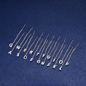 Detail of S999 sterling silver alphabet threader earrings on a navy blue background