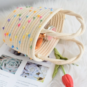 Draufsicht auf eine Baumwollseiltasche mit bunten Pompons auf einem weichen Teppich