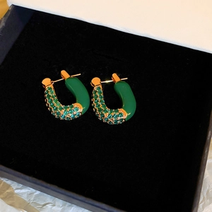 U-shaped gold earrings with emerald enamel and cubic zirconia in a jewelry box