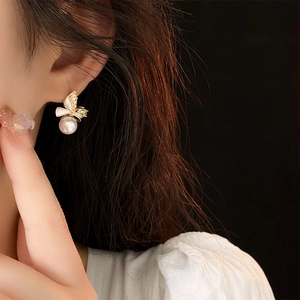 Close-up of gold bow earrings with pearl pendant and zircon stones on a model