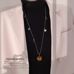 Long silver chain necklace with brown heart gemstone pendant worn over a black sweater