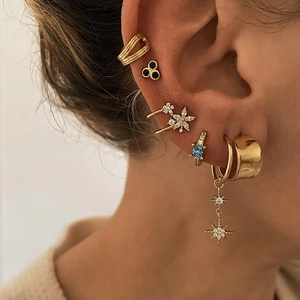 Close-up of layered gold earrings set with blue gemstones and white rhinestones