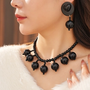 Close-up of black acrylic beaded necklace and heart-shaped tassel earring set on model
