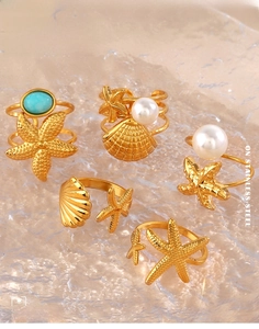 Macro detail of gold starfish and seashell rings with pearls on a textured water background