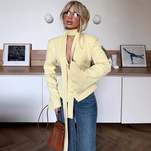 Detail of light yellow slim fit blazer paired with blue jeans and a brown leather bucket bag