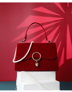 Detail of red velvet handbag with elegant pearl chain and golden heart pendant lock