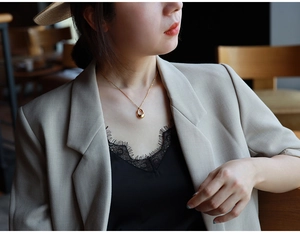 Detail of a gold hollow waterdrop pendant necklace worn by a model in warm light