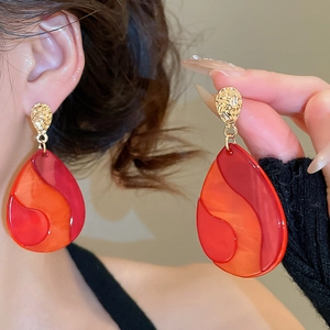 Macro detail of oversized teardrop earrings featuring wavy red resin and hammered gold metal