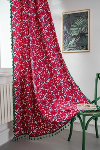Detail of red floral cotton linen curtain with green tassels draped over a chair
