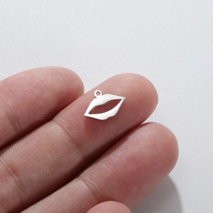 Close-up of silver lip shaped stainless steel pendant held between fingers for DIY jewelry