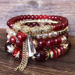 Close-up of Bohemian layered beaded bracelet set with red beads and golden tassel charm