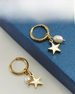 Détail de boucles d'oreilles en or 18K avec perle blanche et pendentifs étoile