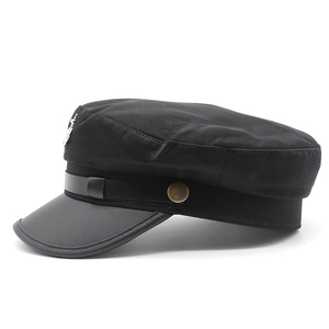 Dettaglio berretto newsboy nero con stemma argento, visiera in pelle e bottoni bronzo
