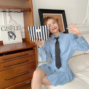 Blue striped makeup bag clutch held by model in a stylish lifestyle setting