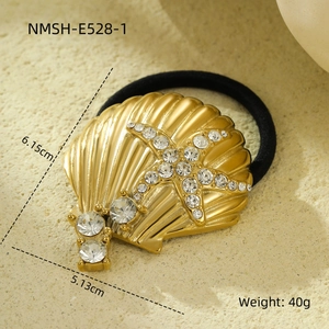 Macro shot of gold shell and rhinestone starfish hair tie on a beige stone background