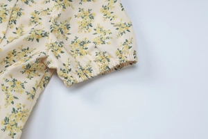 Gros plan sur les poignets élastiques d'une robe plissée à fleurs jaunes sur beige