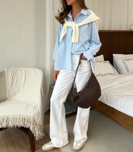 Femme en chemise polo à rayures bleues avec châle en tricot blanc et pantalon large