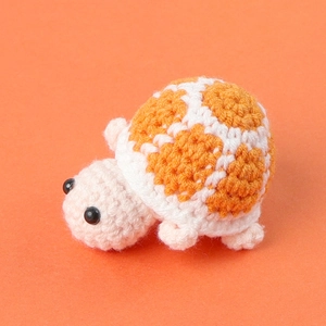 Close-up of a handmade crochet mini turtle doll with orange patterned shell on orange background