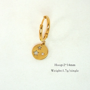 Macro shot of a 14K gold hoop earring with hollow and crystal star pendant on fabric