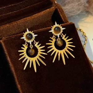 Detailed view of gold sunburst drop earrings with brown tiger eye stone on brown velvet