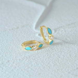 Detail of gold turquoise hoop earrings with marquise blue stones on white rock surface