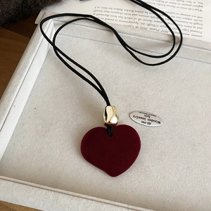 Detail of a red velvet heart pendant with gold accents on a black woven rope necklace