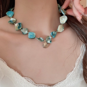Detail of bohemian teal shell bead necklace featuring a golden seashell pendant for women