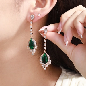 Close-up of elegant rose gold drop earrings with teardrop emerald and white zircon