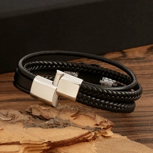 Detail view of men's braided black leather bracelet with silver clasp on rustic wood