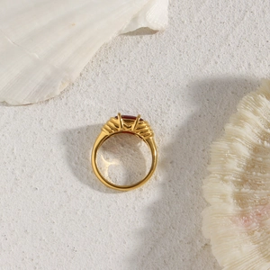 Golden ring with oval reddish-brown gemstone and ribbed band on a sandy surface