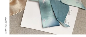 Detailed macro view of gray-green silk scarf with elegant crane prints and satin texture