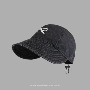 Detailed view of white bow embroidery on black washed denim baseball cap with adjustable strap