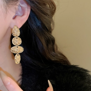 Close-up of gold drop earrings with hammered texture on four tiered oval metal discs