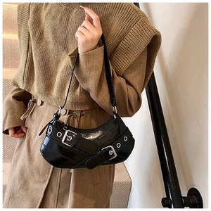 Detail of black punk underarm bag with metal grommets and buckles on shiny faux leather