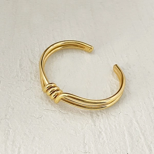 Close-up of gold-plated brass cuff bracelet featuring a triple-line knot design