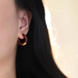Close-up of model wearing burgundy and gold enamel hoop earrings in 18K plated titanium