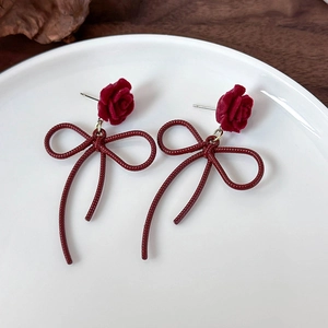 Elegant velvet red rose earrings with long ribbon bow on white ceramic tray