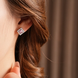 Macro detail of square silver earring with pink zircon stone worn on a model's ear