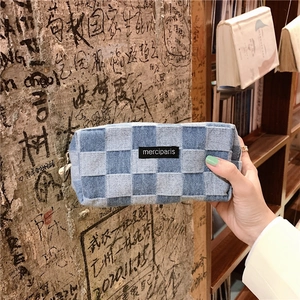 Detail of checkered denim pencil case with black logo patch and durable metal zipper