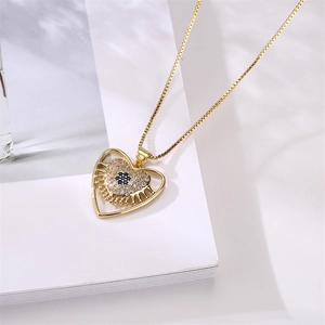 Close-up of gold plated heart pendant with zircon evil eye on a white book surface