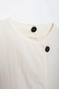 Detailaufnahme der cremefarbenen Pufferjacke mit Kragen und schwarzen Knöpfen