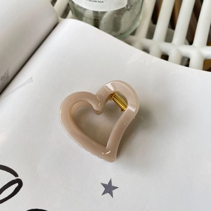 Detail view of coffee cream heart claw clip with golden spring on white book pages
