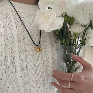 Minimalist gold heart pendant necklace on black cord worn over white knit sweater