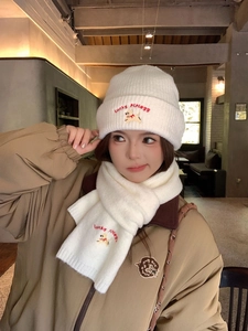 Close-up of white knit beanie and scarf set with lucky dog embroidery and ribbed texture